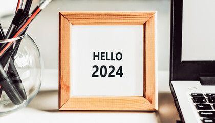 Hello 2024 printed on a white card in wooden frame, on an office desk.