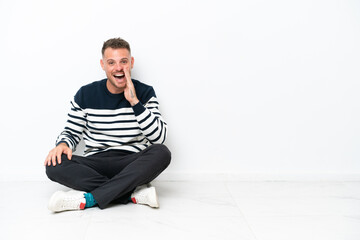 Young man sitting on the floor isolated on white background shouting with mouth wide open