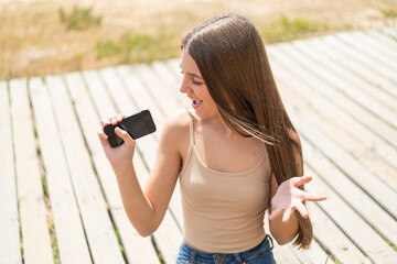 Teenager girl at outdoors using mobile phone and singing