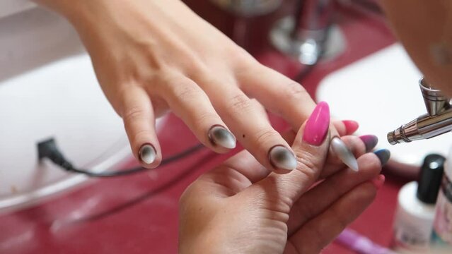 Closeup shot of a woman in a nail salon receiving a manicure by a beautician with airbrush. Woman getting nail manicure