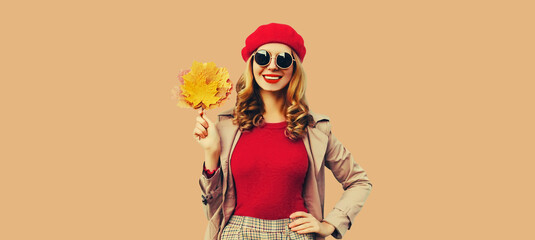 Autumn color style outfit, portrait of beautiful smiling young woman with yellow maple leaves wearing red french beret hat, jacket on brown studio background