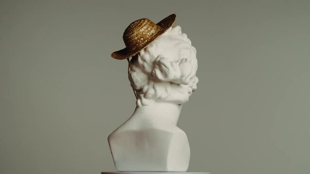 Closeup shot. Ancient marble bust statue of roman era woman in small straw hat spinning on a platform. Isolated on grey background.