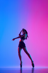Beautiful female dancer wearing bodysuit and heels while performing pole dance tricks in colorful neon light