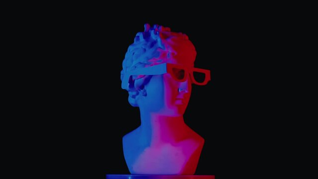 Closeup shot. Ancient marble bust statue of roman era woman in 3d glasses spinning on a platform in red blue neon lights. Isolated on black background.