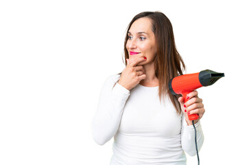 Middle age woman holding a hairdryer over isolated chroma key background thinking an idea and looking side