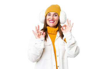 Middle age woman wearing winter muffs over isolated chroma key background showing an ok sign with fingers