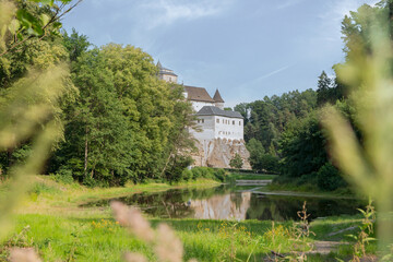 Fototapeta na wymiar The castle with a pond, photographed from the bush, evokes the coolness of a summer day and invites you to hikes and adventures.