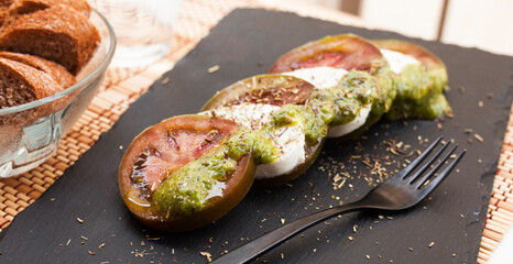 Caprese salad with mozzarella, black tomatoes and pesto on black stone plate