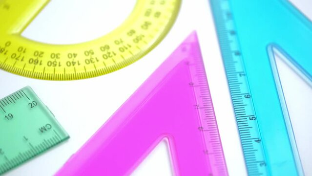 rotation of bright plastic school supplies for studying geometry and mathematics, triangle, ruler, protractor on a white background. closeup.