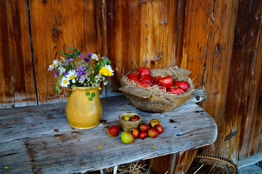 rustic countryside scenery with an old yellow vase with field flowers and red apples in the basket on the wooden bench in the Bavarian village Schwangau, Bavaria, Germany