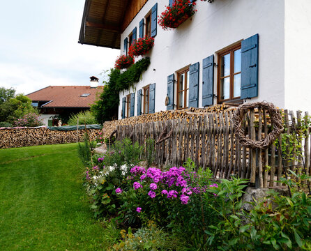 idyllic scene with a traditional Bavarian rustic alpine farmhouse with red geraniums and a firewood pile by the wall in Schwangau in the Bavarian Alps on summer day (Bavaria, Germany) 