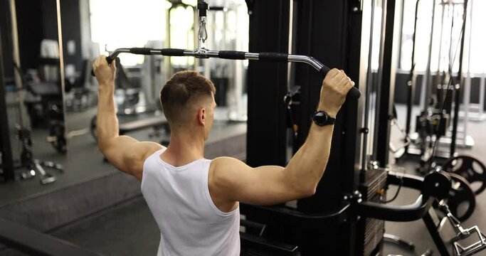 Young man is engaged in gym. Man pulling bar down