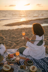Young woman having beautiful tasty picnic with lemonade, fresh fruits and croissants on a beach at sunset.