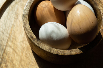 A natural farm product is one of the main ones in the form of chicken eggs with shells of different colors. Chicken eggs on a wooden plate, side view close-up photo.