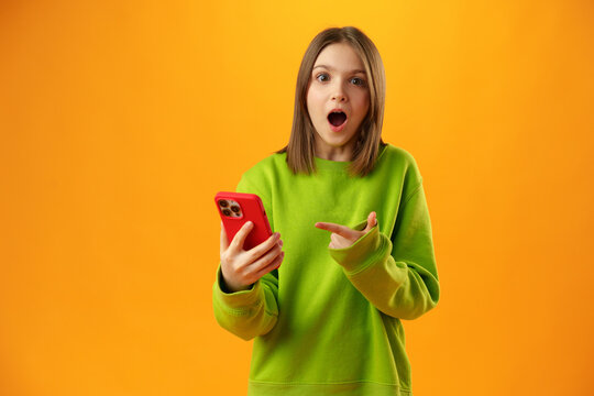 Surprised Teen Girl Using Mobile Phone Against Yellow Background