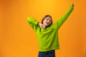 Portrait of a joyful happy teenage girl celebrating success on yellow background