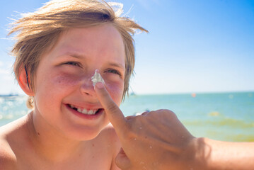 portrait of a happy boy with a cream on his nose, a child on a summer vacation at the sea. parent, mom puts sunscreen on son's face on the beach.