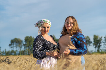 Front view of two caucasian plus size women standing next to each other on agricultural wheat field with ripe ears of wheat in a summer sunny day. Soft focus. Golden hour. Female friendship theme.