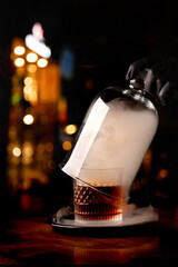 opening drink smoker from a glass of smoked cognac with smoke on blurred pub wooden table