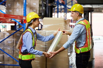 factory workers or warehouser wrapping stretch film parcel on pallet covered cardboard boxed in warehouse storage