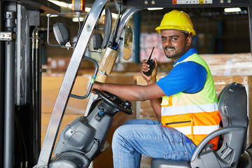 Indian worker driving a forklift and holding wireless radio in warehouse storage