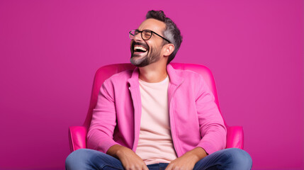 Young man laughs against a pink background.