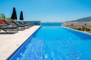 Obraz premium Summer vacation at poolside. Veranda decorated with deck chairs and umbrella with an ocean view