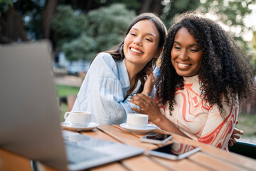 Portrait of happy young multiethnic female friends using laptop in cafe outdoors