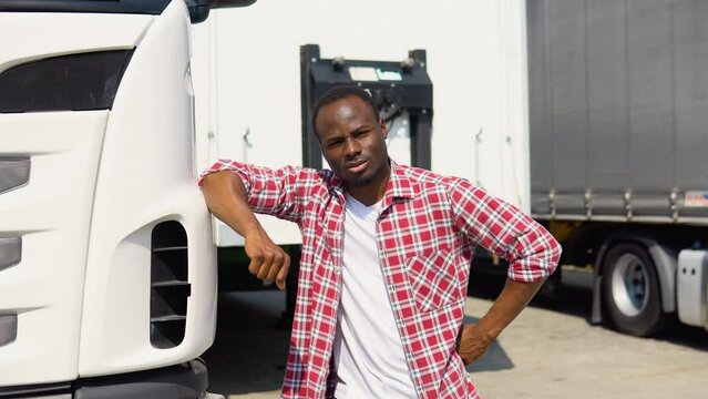Portrait of african american truck driver standing near his truck on parking lot looking at camera. Copy space