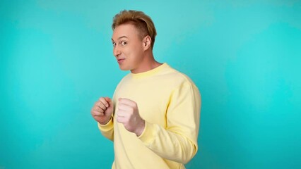 Positive man dancing having fun rhythm to music, enjoying life, entertainment. Carefree guy excited dance in a yellow sweatshirt. Studio shot isolated on blue background.