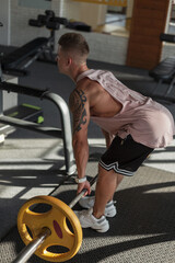 Fototapeta na wymiar Handsome muscular healthy man in sportswear doing an exercise with weights in the sport gym