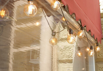 Decorative garland of retro light bulbs hangs on the facade of a street cafe