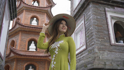 Portrait of Asian Vietnamese woman with Vietnam dress and straw hat in Tran Quoc temple pagoda. Tourist attraction landmark in urban city town of Hanoi, Vietnam. People lifestyle.