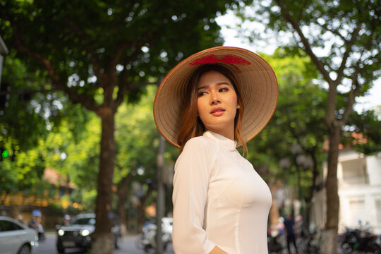 Portrait of Asian Vietnamese woman with Vietnam dress and straw hat in tree corridor in Hanoi. People lifestyle.