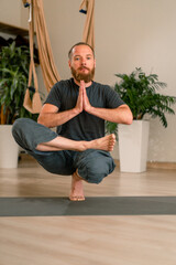 focused adult male yogi with a beard performs a pose exercise from yoga meditates and keeps balance...