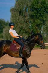 Foto op Canvas A horsewoman dressed in a helmet rides her beautiful black horse in a horse riding arena during a horseback ride © Guys Who Shoot