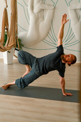 a male yogi with a beard does back stretching on the floor in a beautiful yoga studio to improve...