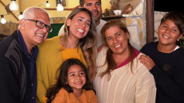 Hapy latin family smiling on camera during night time - Grandparents, parents and children 
