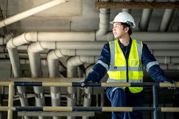 Confident man construction worker with reflective green vest and protective safety helmet. holding...