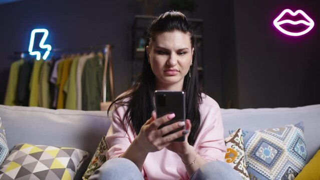 Irritated young woman using smartphone. Woman see unpleasant news, photos, videos online in internet, aggressively scrolls through disgusting content with revulsion, loathing, sense of sickening.