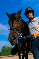 Obraz premium A horsewoman in a helmet hugs and scratches her beautiful black horse with her hand at the equestrian arena during a horseback ride
