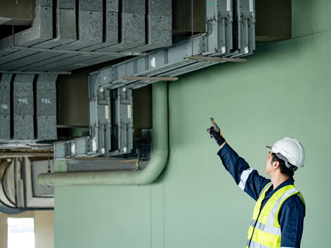 Building inspector man checking telephone cable duct wireway. Asian male maintenance worker with reflective vest and safety helmet pointing at wire way working for communication system inspection