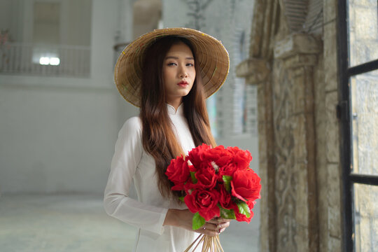Portrait of Asian Vietnamese woman with Vietnam dress and straw hat, bouquet flower in Hanoi. People lifestyle.
