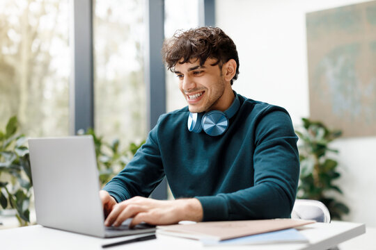 Cheerful european guy using laptop, watching online lesson or webinar, sitting in modern university audience