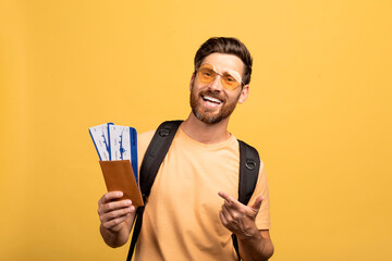 Traveling by air concept. Happy european middle aged man pointing at passport and airplane tickets on yellow background