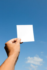 Mão de homem branco segurando papel branco com fundo céu azul