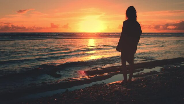 Woman silhouette against amazing colorful sunset sky over ocean waves. Slim girl stand on coast beach relax and enjoy wild nature beauty on tropical island. Travel, tourism, holiday, active lifestyle