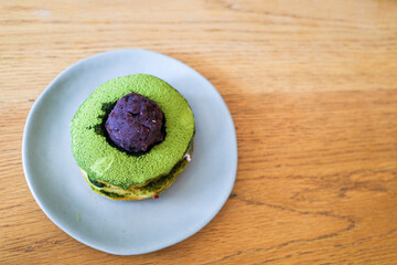 Matcha green tea-filled donut with  red bean paste in blue plate on wooden table from above in copy space concept.