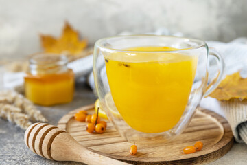 Relaxation and herbal medicine. Hot herbal vitamin sea buckthorn tea in a glass cup with fresh sea buckthorn berries, honey and lemon on a stone tabletop.