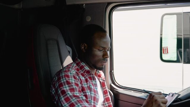 African american delivery man with cardboard box checking list in truck. Courier checking list on clipboard
